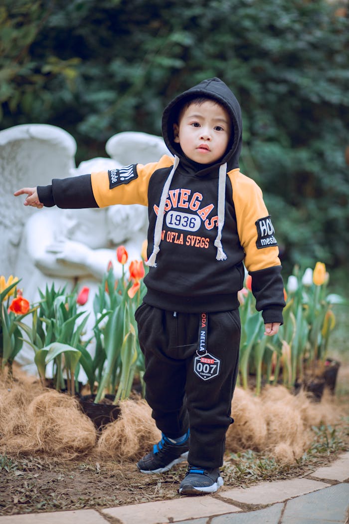 creative-03 Young child in a black hoodie poses in a garden, surrounded by flowers and a statue.