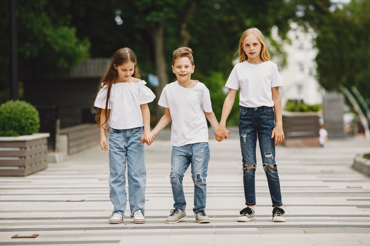 brand-02 Three children in white t-shirts and jeans holding hands outdoors on a summer day.
