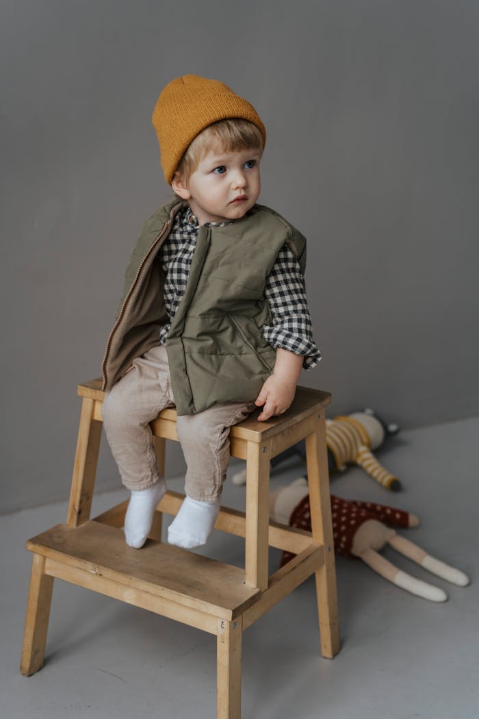 Services-03 Cute child wearing beanie and winter clothes, sitting on wooden stool in indoor studio setting