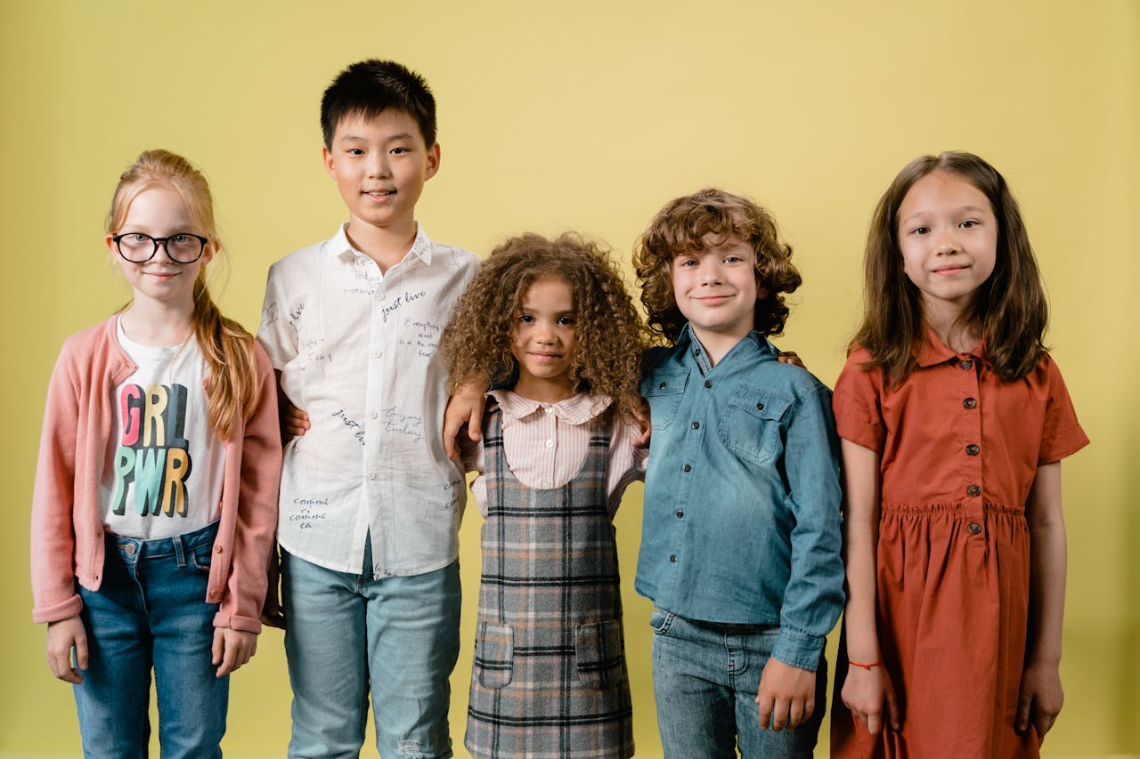 creative-02 Five diverse children smiling against a yellow background in a studio setting.