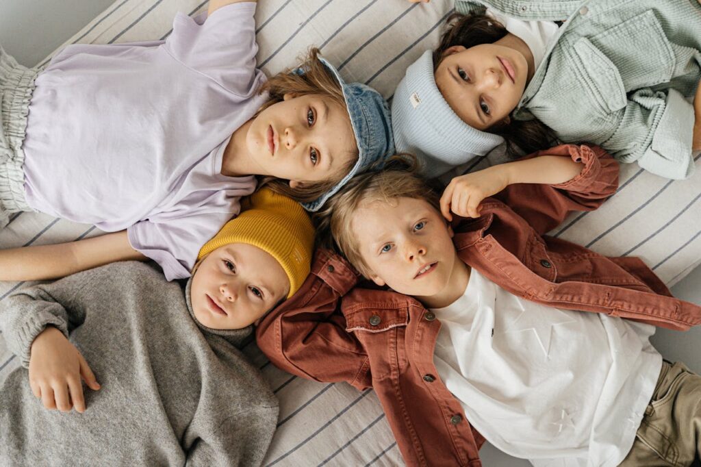 Four children in colorful outfits lying on a bed, displaying playful and relaxed expressions.