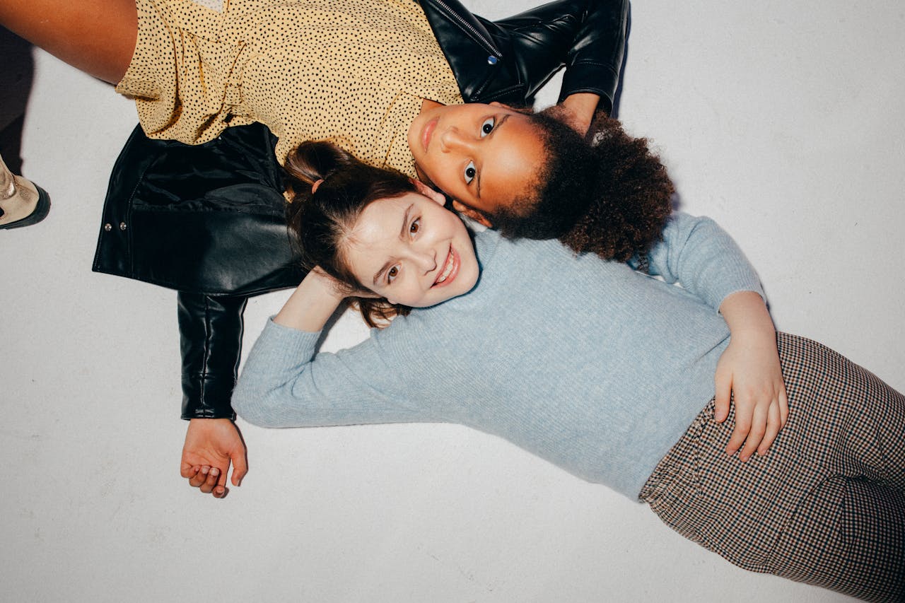 Two cheerful children lying down, showcasing friendship and diversity with genuine smiles.