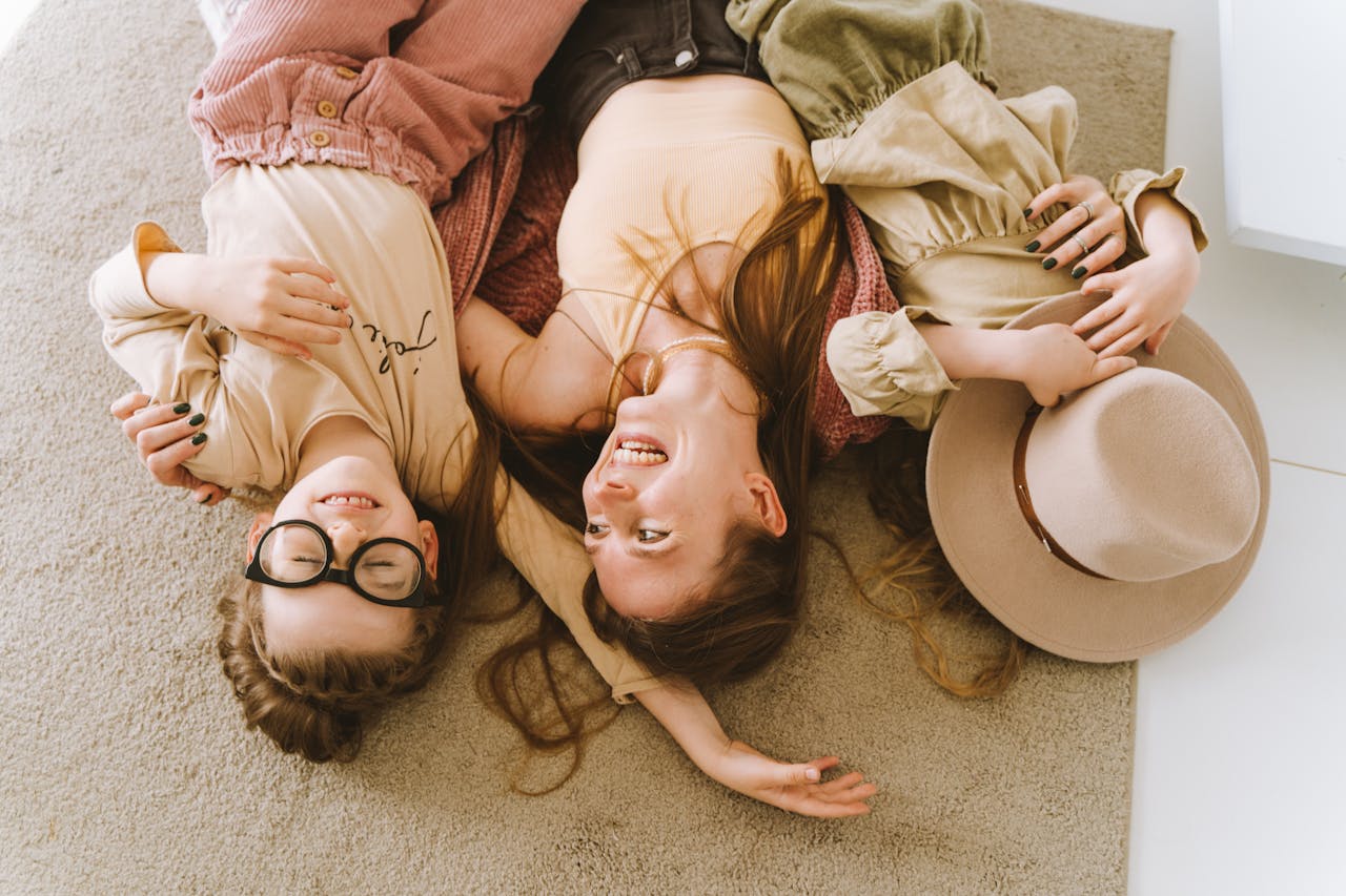 Mother and daughters lying happily on the carpet, embracing and smiling.